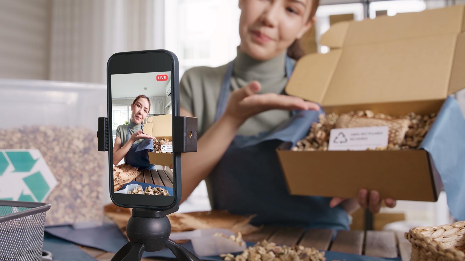 Female influencer unboxing product in front of phone on tripod