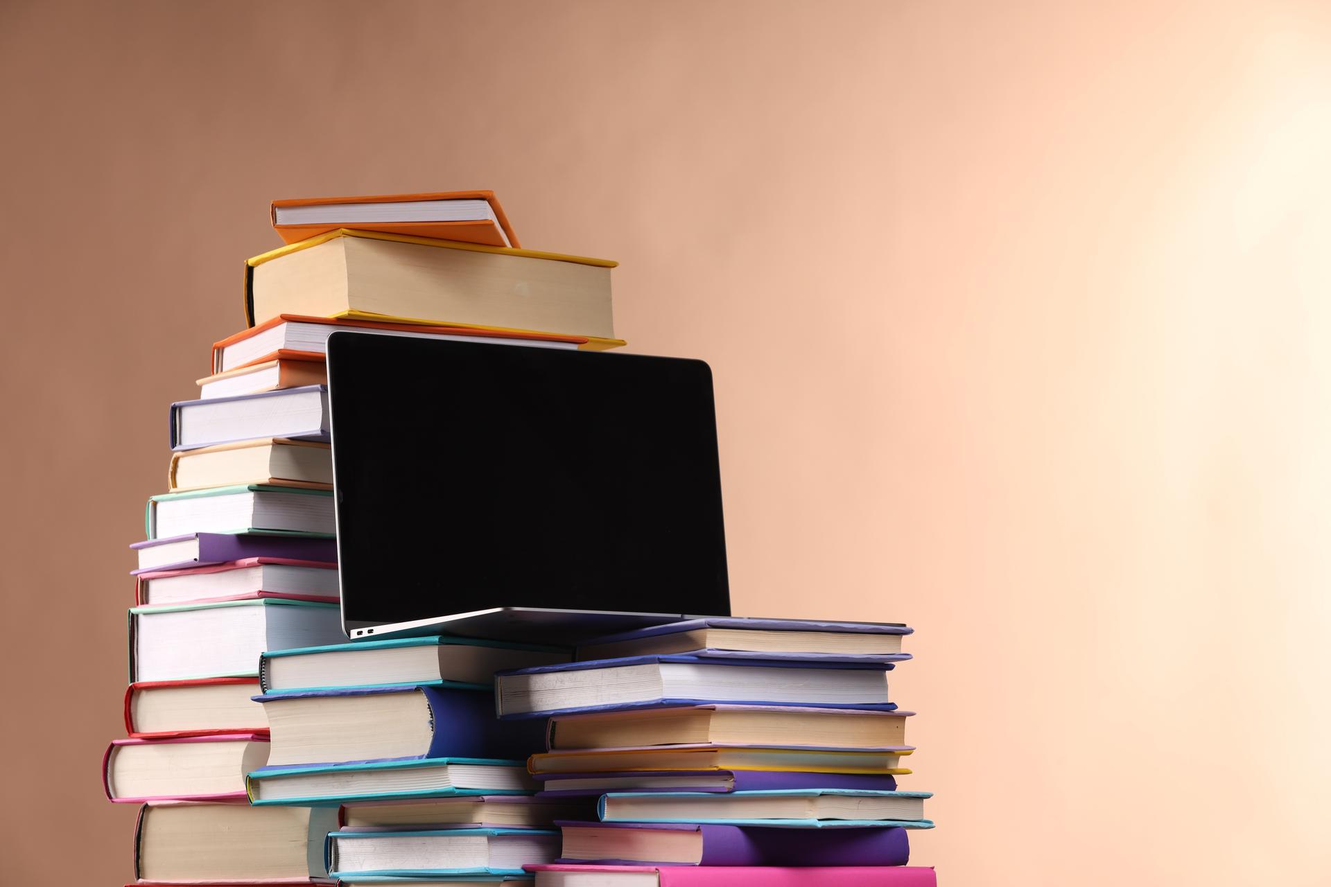 Stack of colorful books and a laptop, illustrating web publishing in a digital age