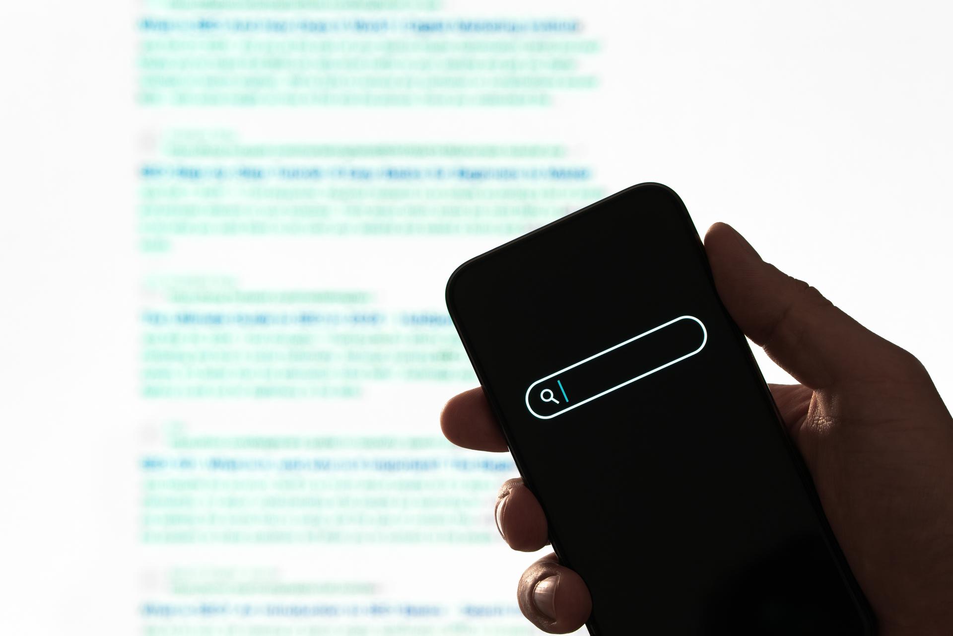 Hand Holding Smartphone for Search Results A hand holding a smartphone showing a blurred web search screen, highlighting digital search evolution.