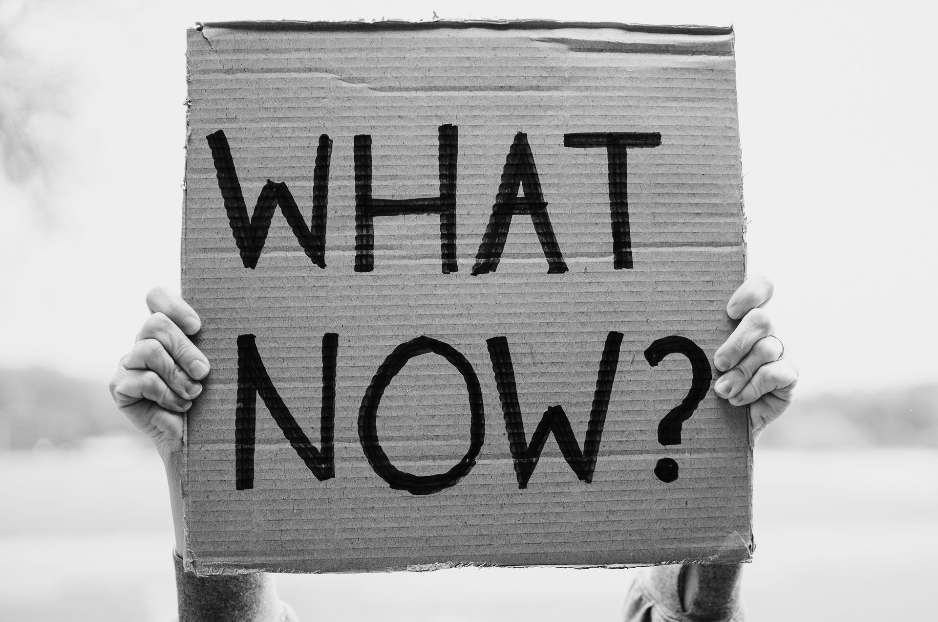 Person holding a “WHAT NOW?” sign about AI advertising trust after a purchase