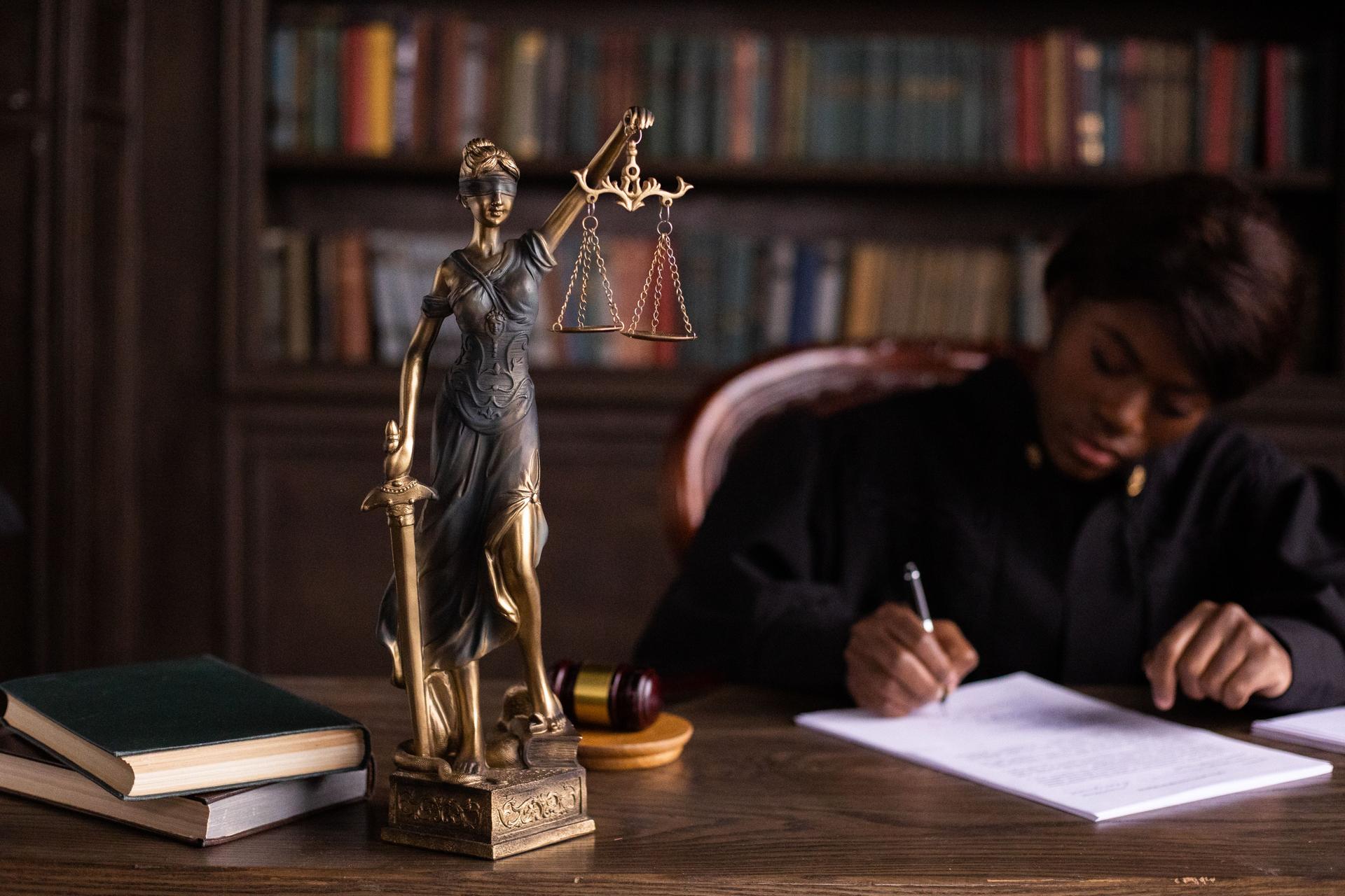 Lady Justice and Court Proceedings Amid AI Concerns Judicial figure surrounded by items representing legal proceedings, highlighting issues caused by AI misuse in courts
