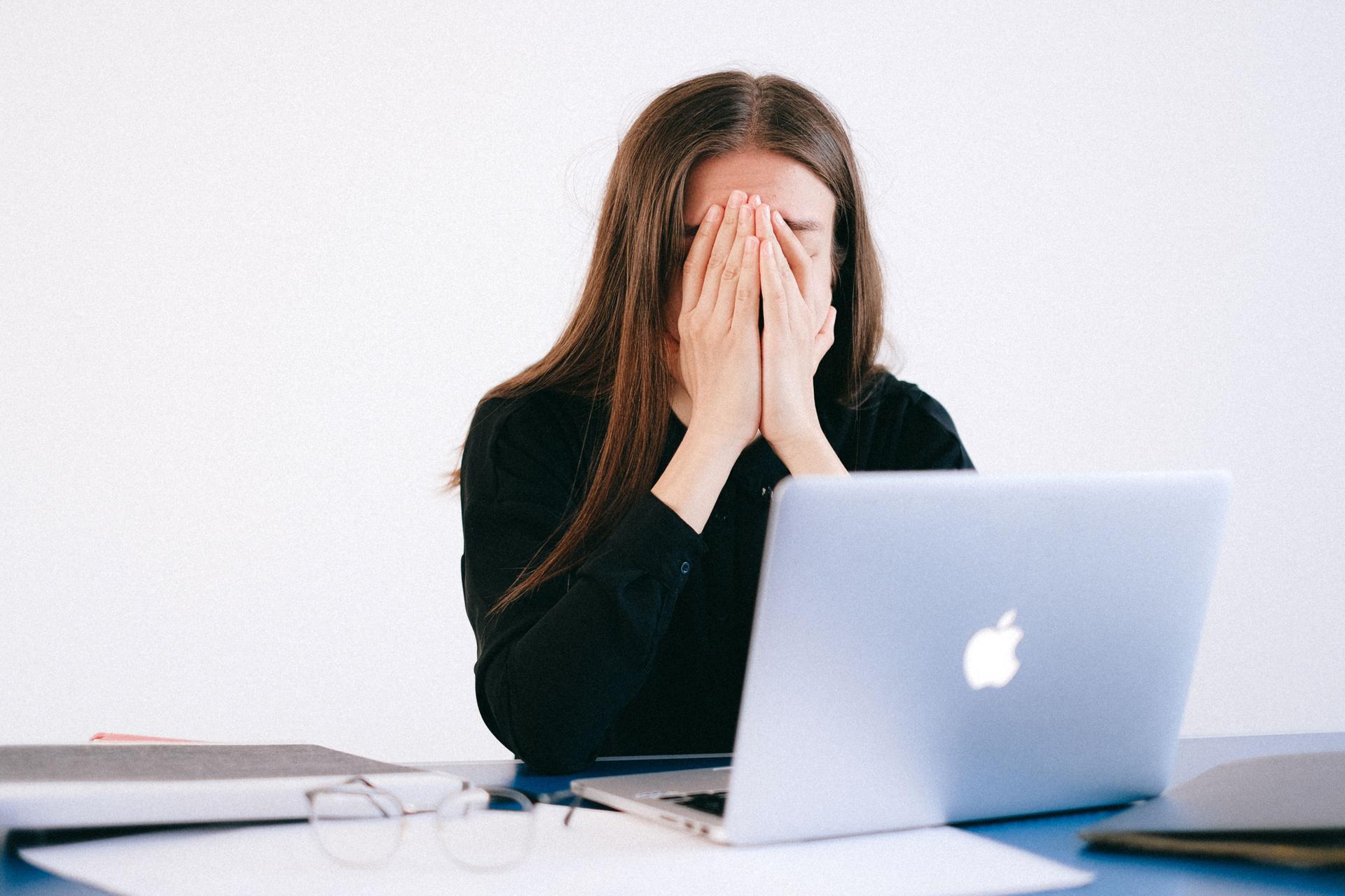 Woman covering her face at a laptop, reflecting stress over OpenAI's opaque firings and safety culture