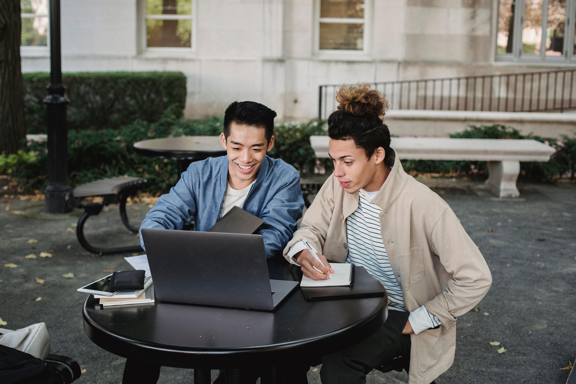 Two young men collaborating on college studies using a laptop outdoors, ideal for ChatGPT's educational tools