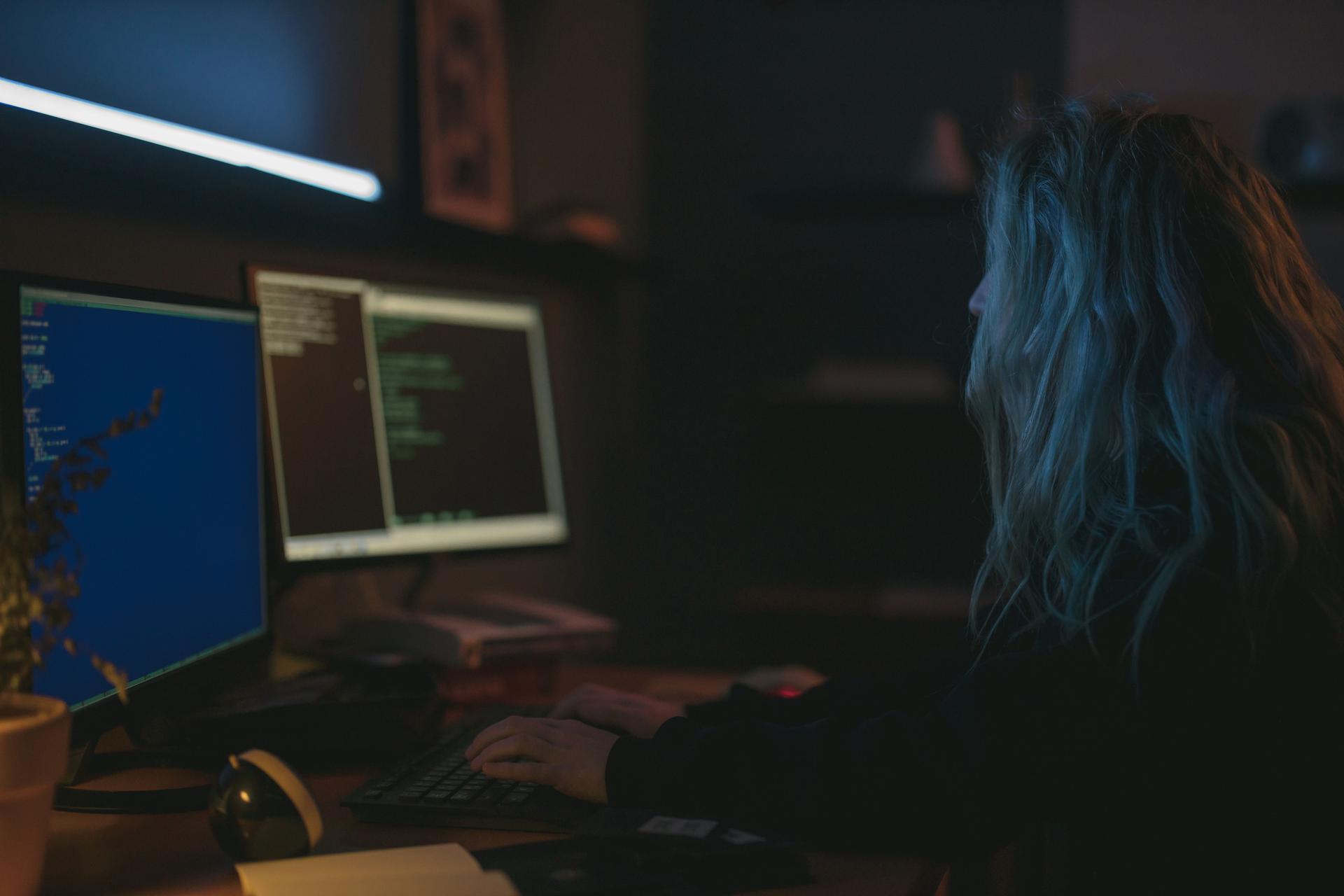 A woman analyzing data on dual monitors reflecting AI hacking incidents discussions.