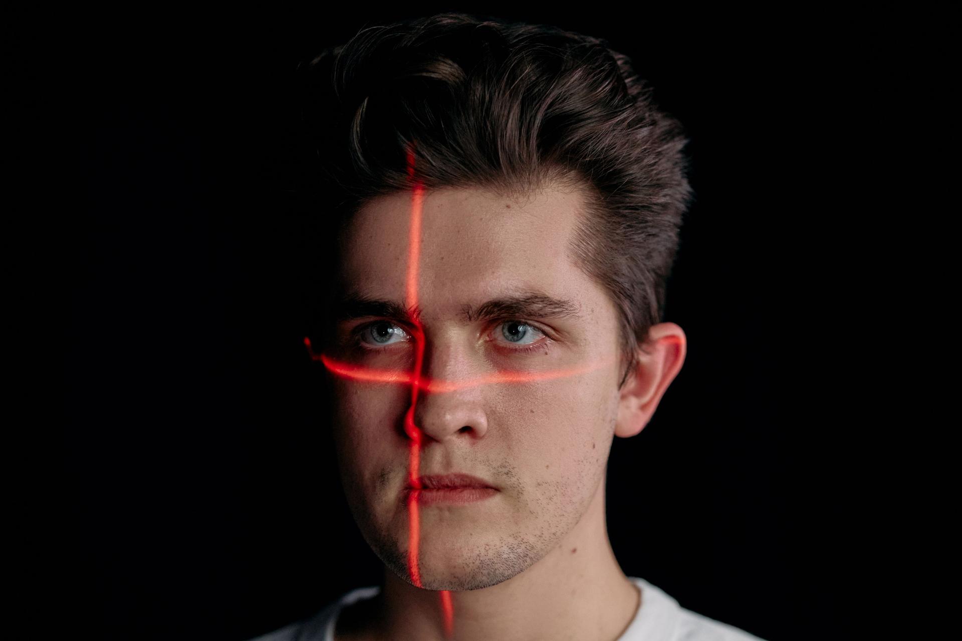 Young man with laser lines on his face, highlighting the manipulation of digital imagery related to deepfake ads.